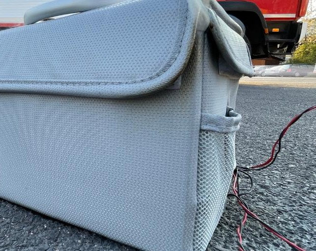Vlitex Battery Safety Box during the real fire test in front of a fire apparatus, with charging cables leading into the box