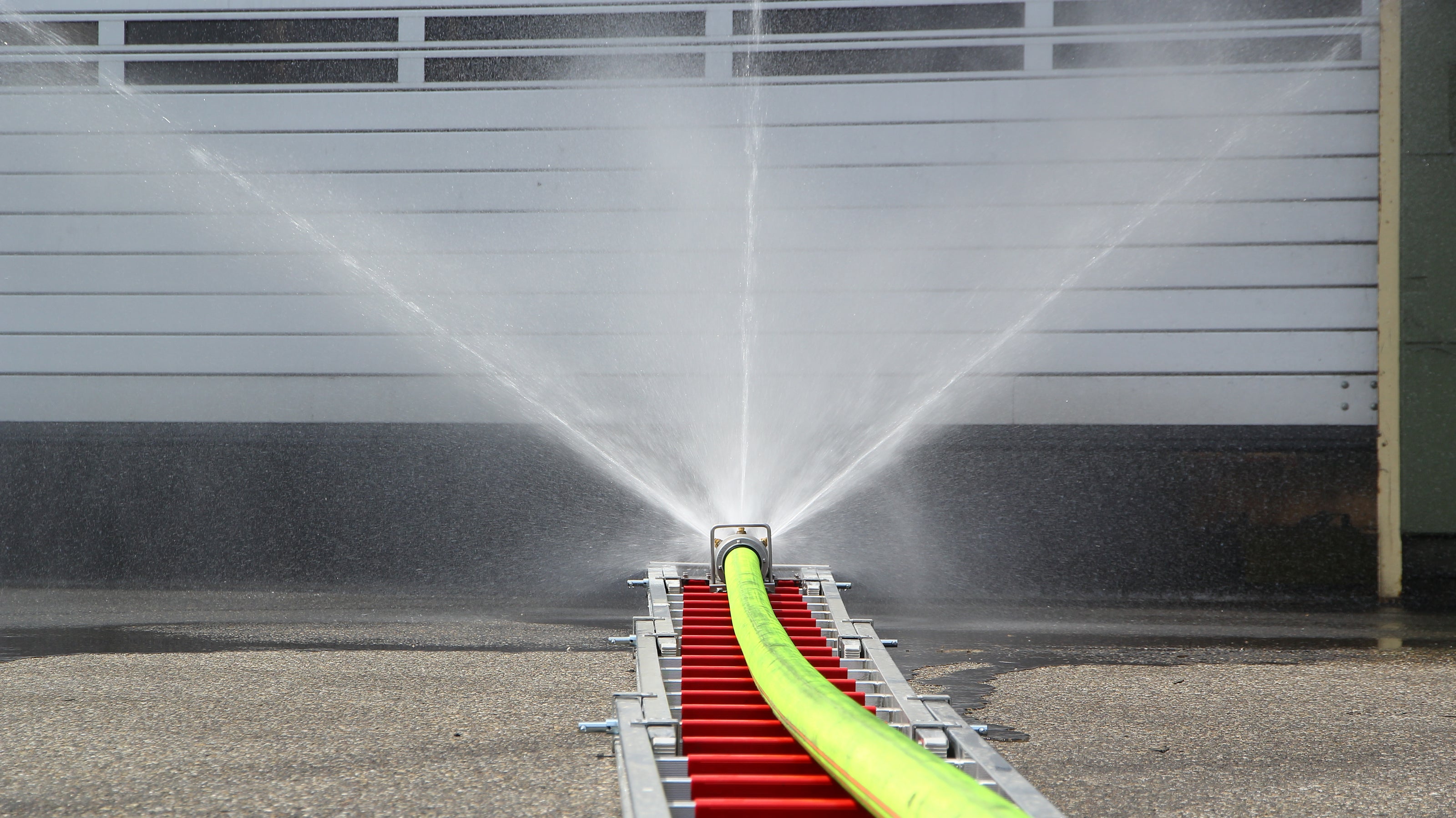 Innovative Feuerwehrtechnik wie der Löschigel auf einer Feuerwehr-Steckleiter vor einer brennenden Industriehalle.