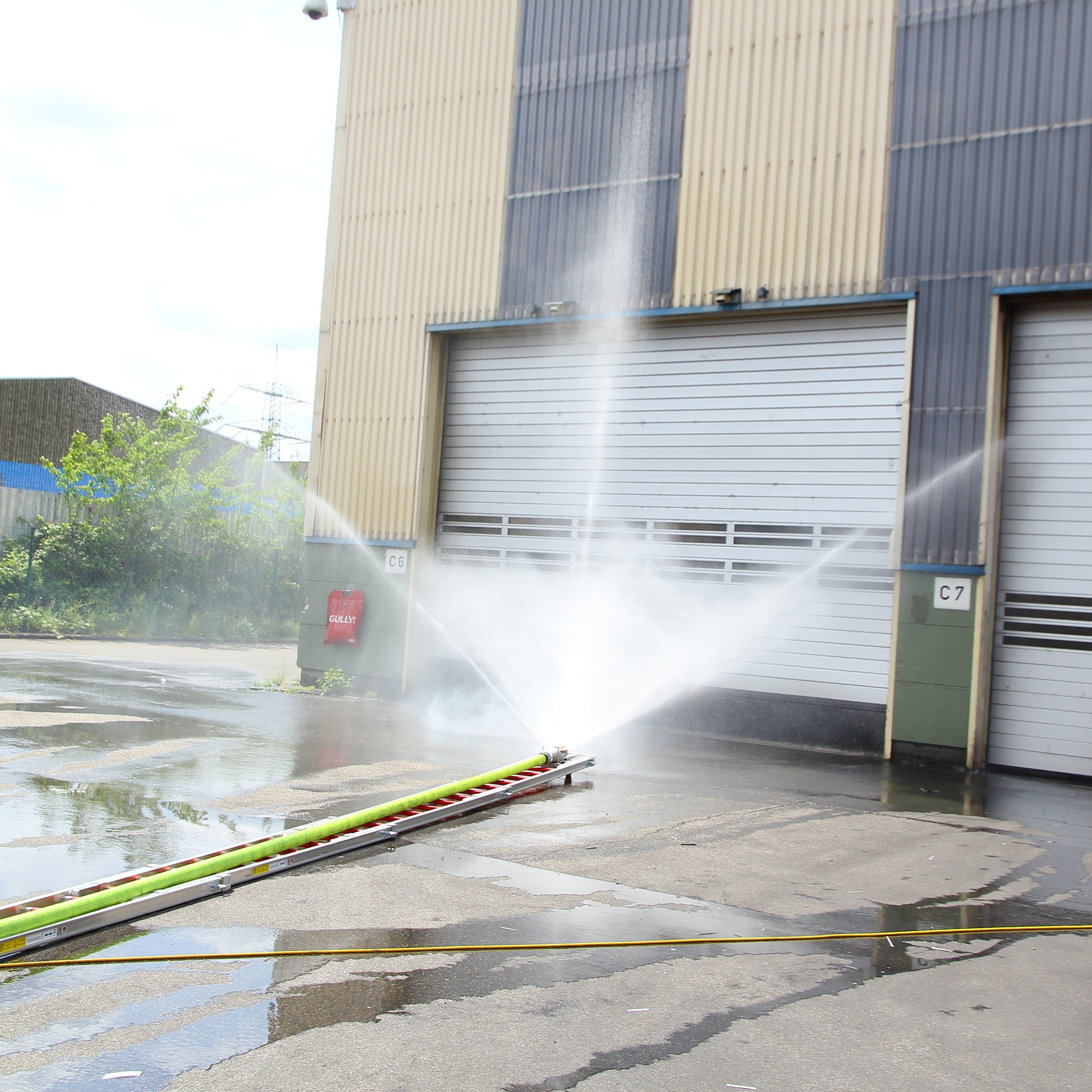 Innovative Feuerwehrtechnik wie der Löschigel auf einer Feuerwehr Steckleiter wie er von einer Werkfeuerwehr in eine brennende Industriehalle geschoben wird.