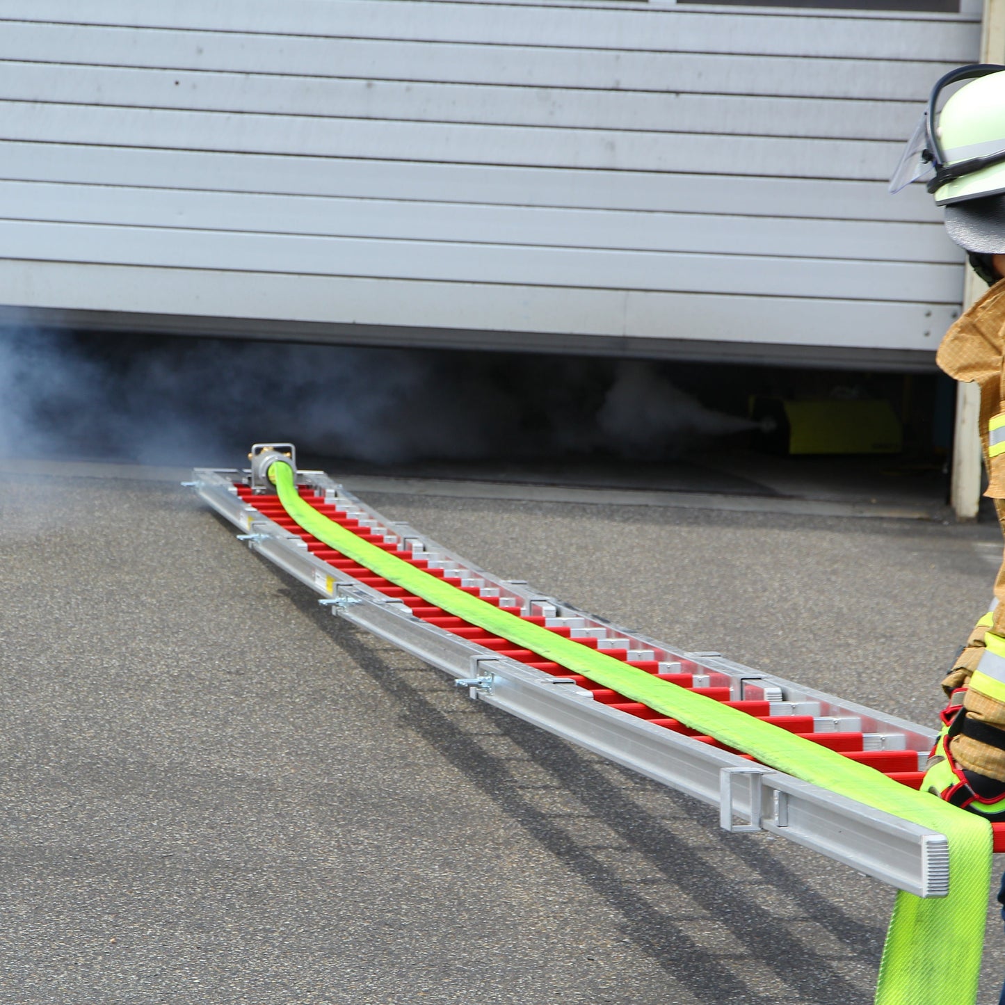 Der Feuerwehr Löschigel wie er von einem Feuerwehrmann auf einer Steckleiter in einen Industriebrand geschoben wird um den Lagerhallenbrand zu löschen