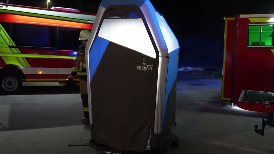 Beleuchtete easyToilet SOS bei Nacht neben Feuerwehrfahrzeugen, eine Einsatzkraft geht zur Tür